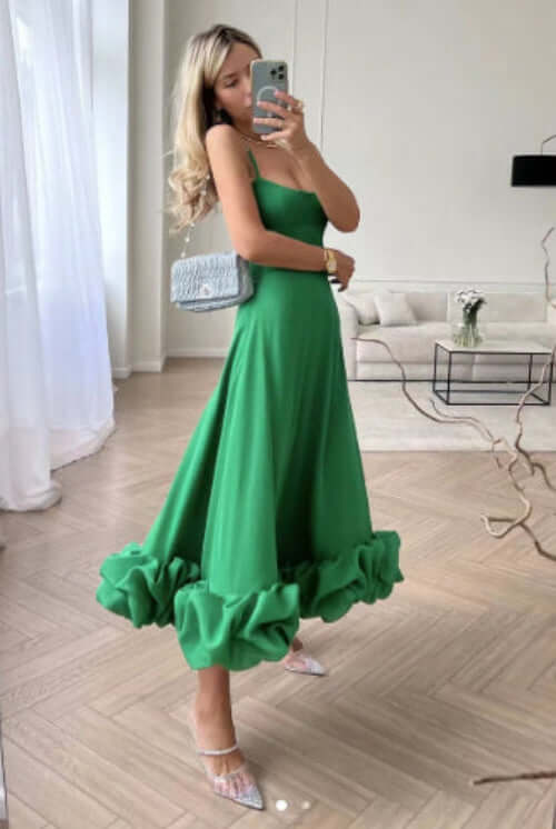 Woman in a vibrant green A-line dress with ruffled hem and straps, showcasing a stylish summer look.