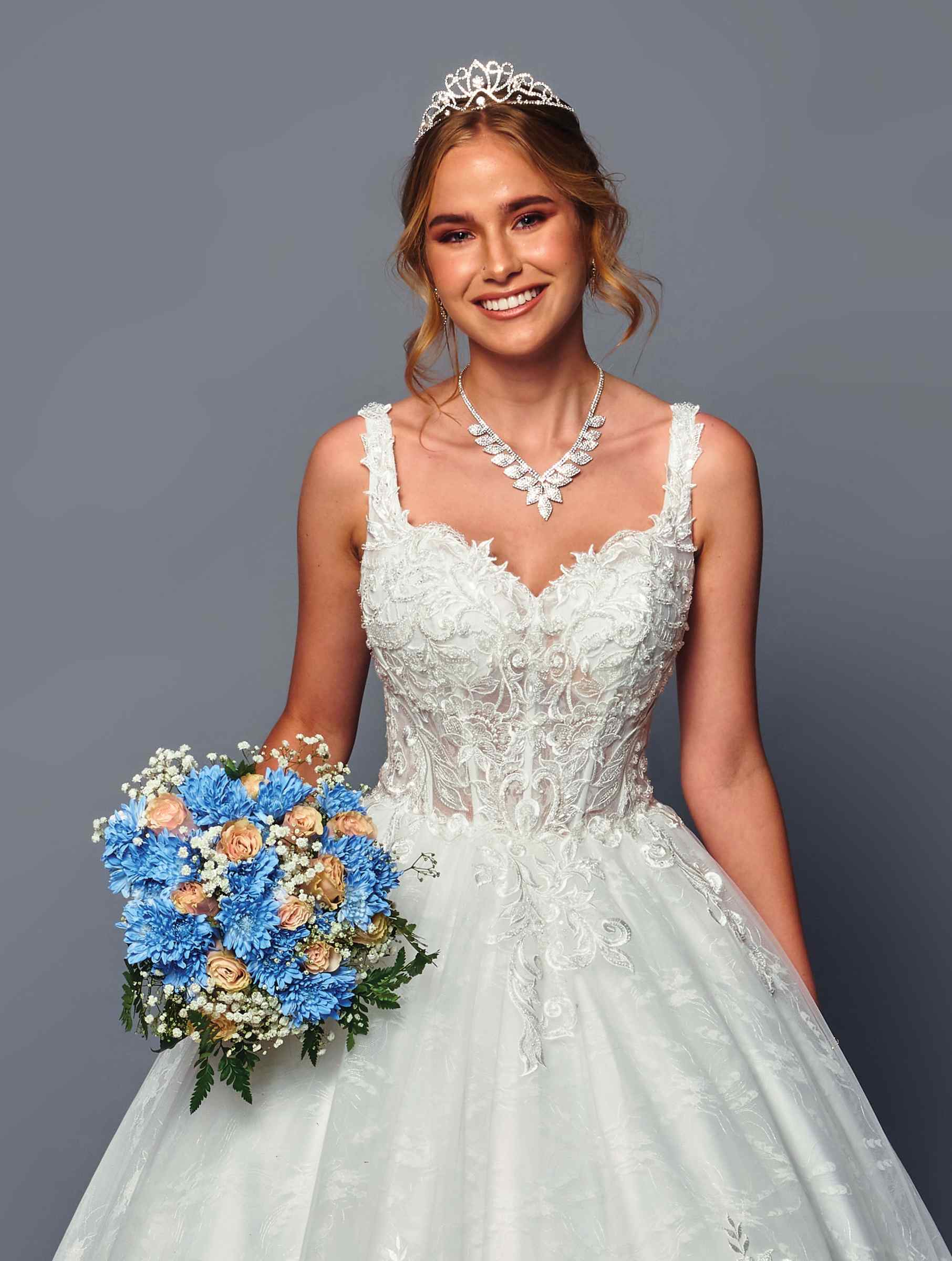 Woman in a white wedding dress holding a bouquet against a gray background