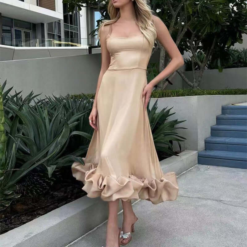 Model wearing a light beige dress with ruffled hem, standing outdoors amidst lush greenery.