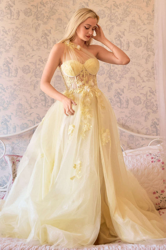 Woman wearing a yellow evening gown with floral details against a decorative wall.