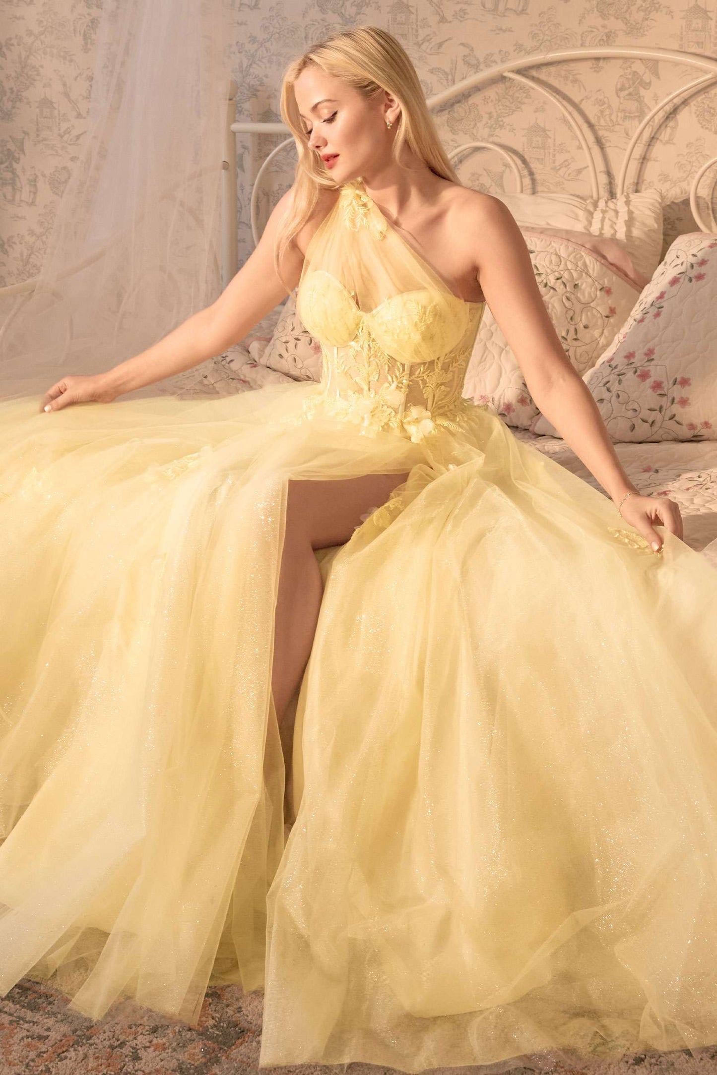 Woman in a yellow evening gown sitting on a decorative bed.