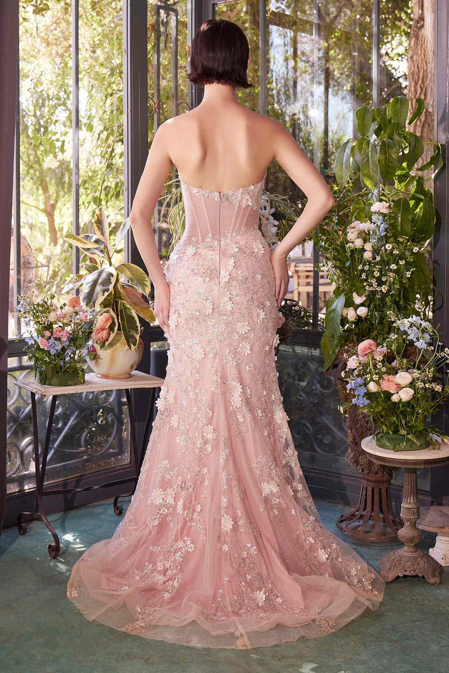 Woman in a pink strapless gown standing in a decorated room with flowers and greenery.