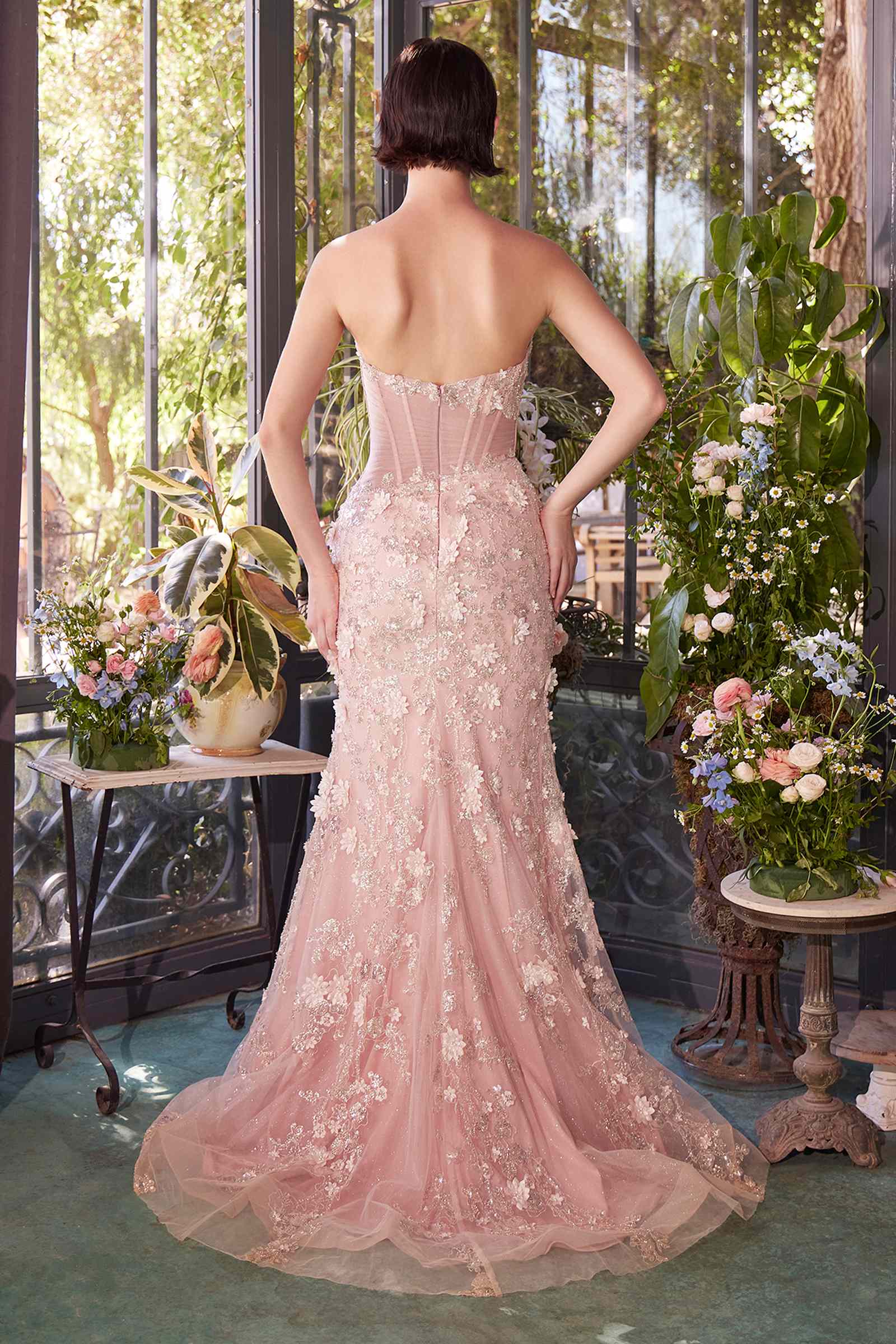 Woman in a pink strapless gown standing in a decorated room with flowers and greenery.