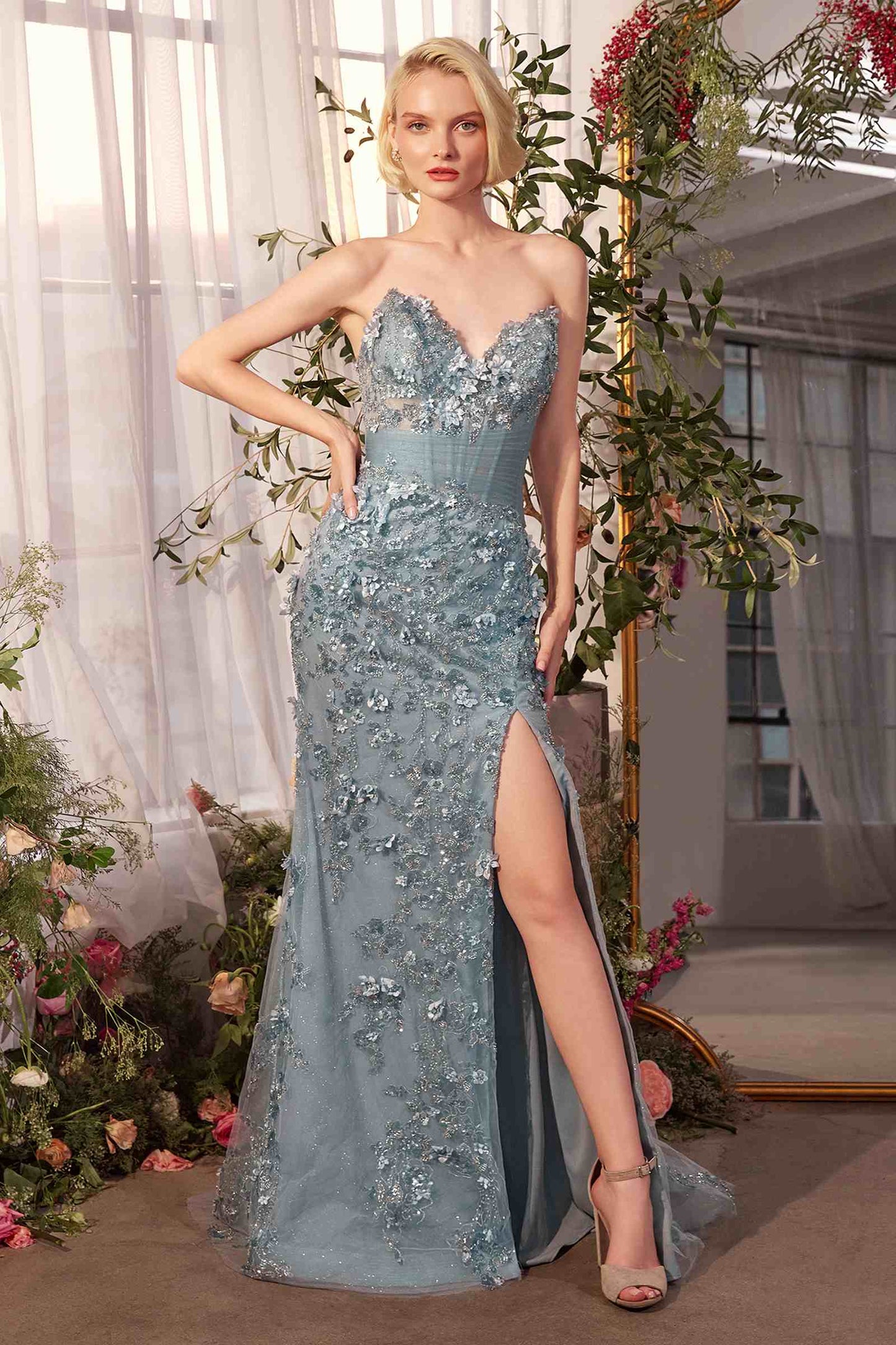 Woman in a light blue evening gown with floral embellishments standing in a decorated indoor setting.