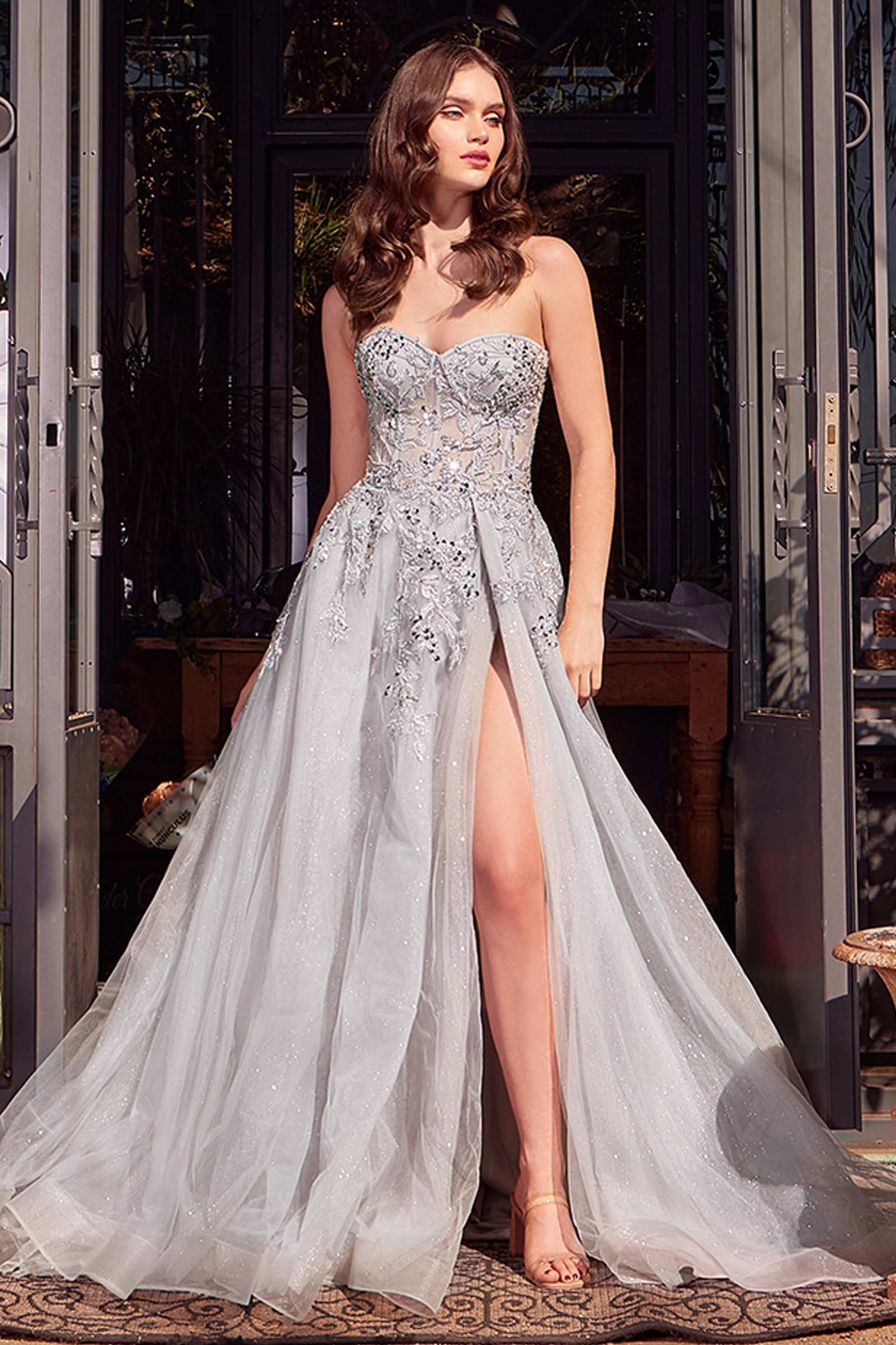 Woman wearing a silver strapless gown with a high slit in a decorated room.