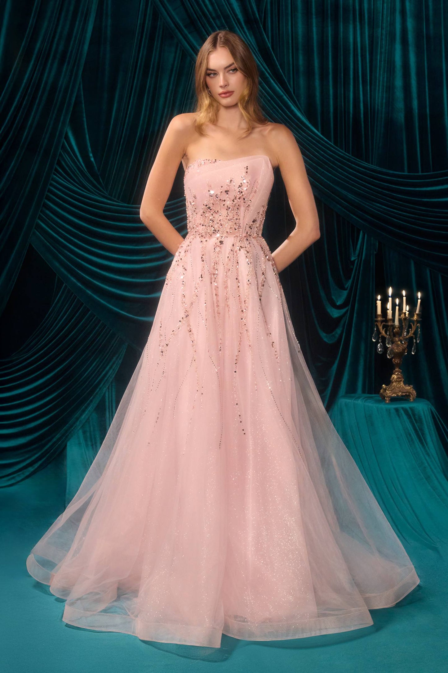 Woman in a pink strapless gown with floral embellishments against a teal curtain backdrop.
