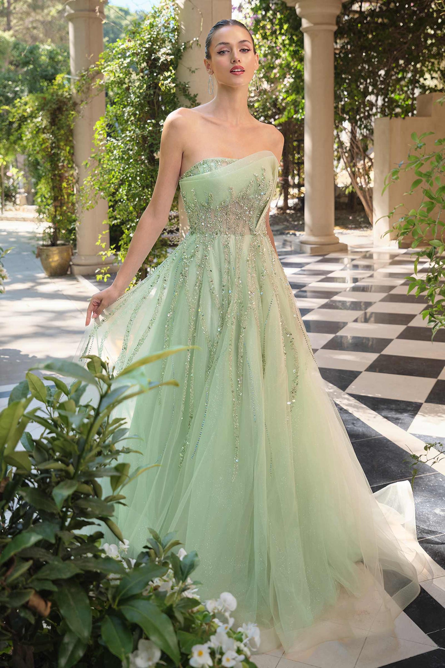 Woman in a light green strapless gown standing outdoors with columns and plants in the background