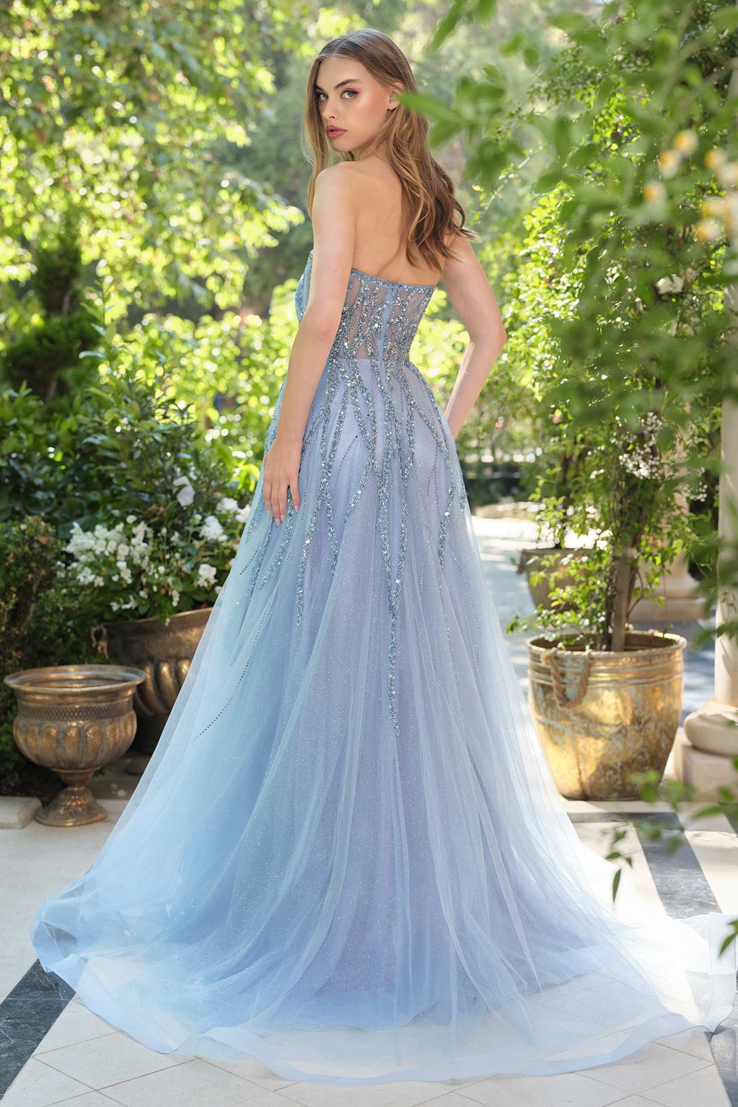 Woman in a light blue evening gown standing outdoors with greenery around