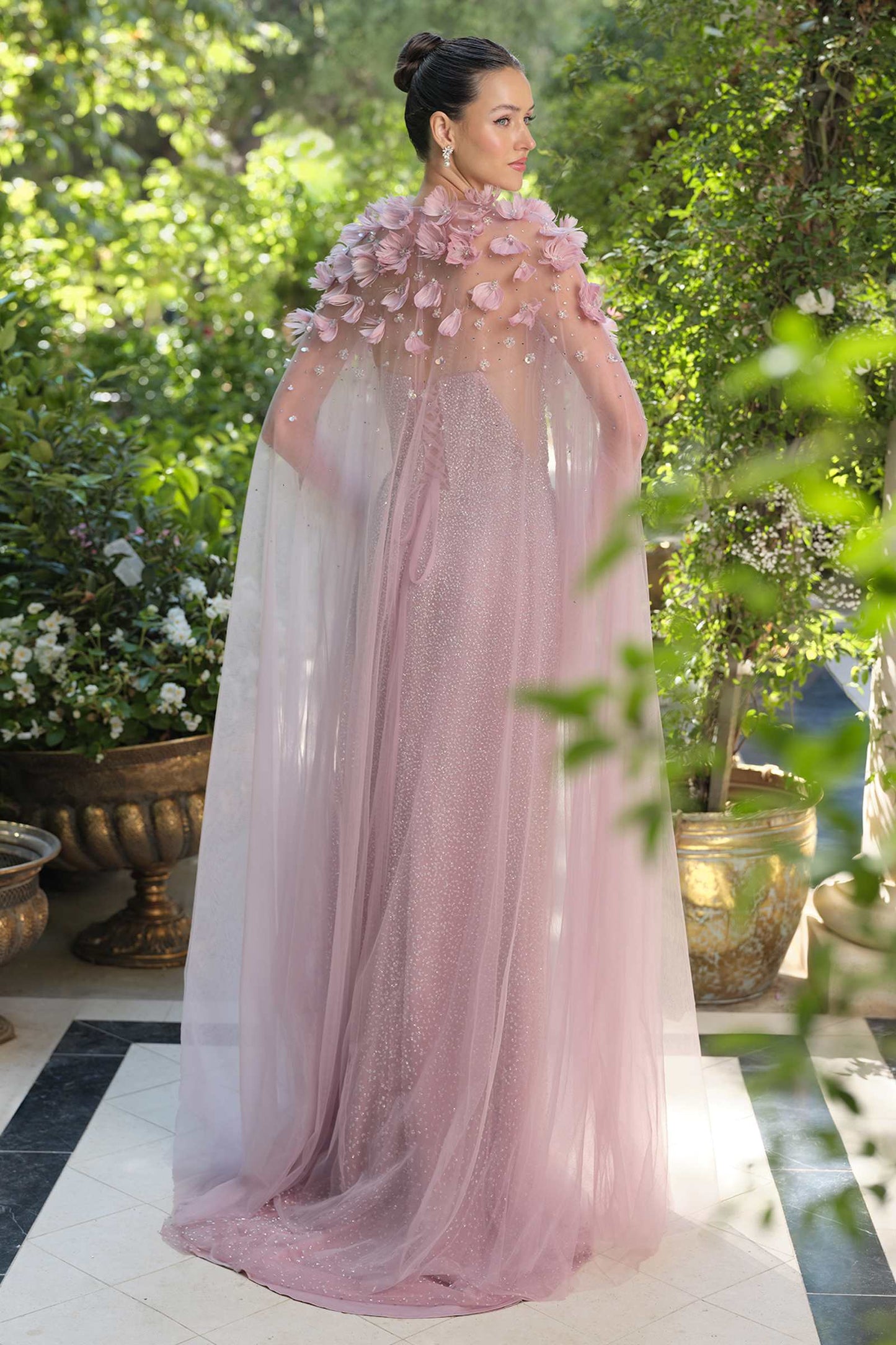 Woman in a pink floral gown standing outdoors with greenery in the background