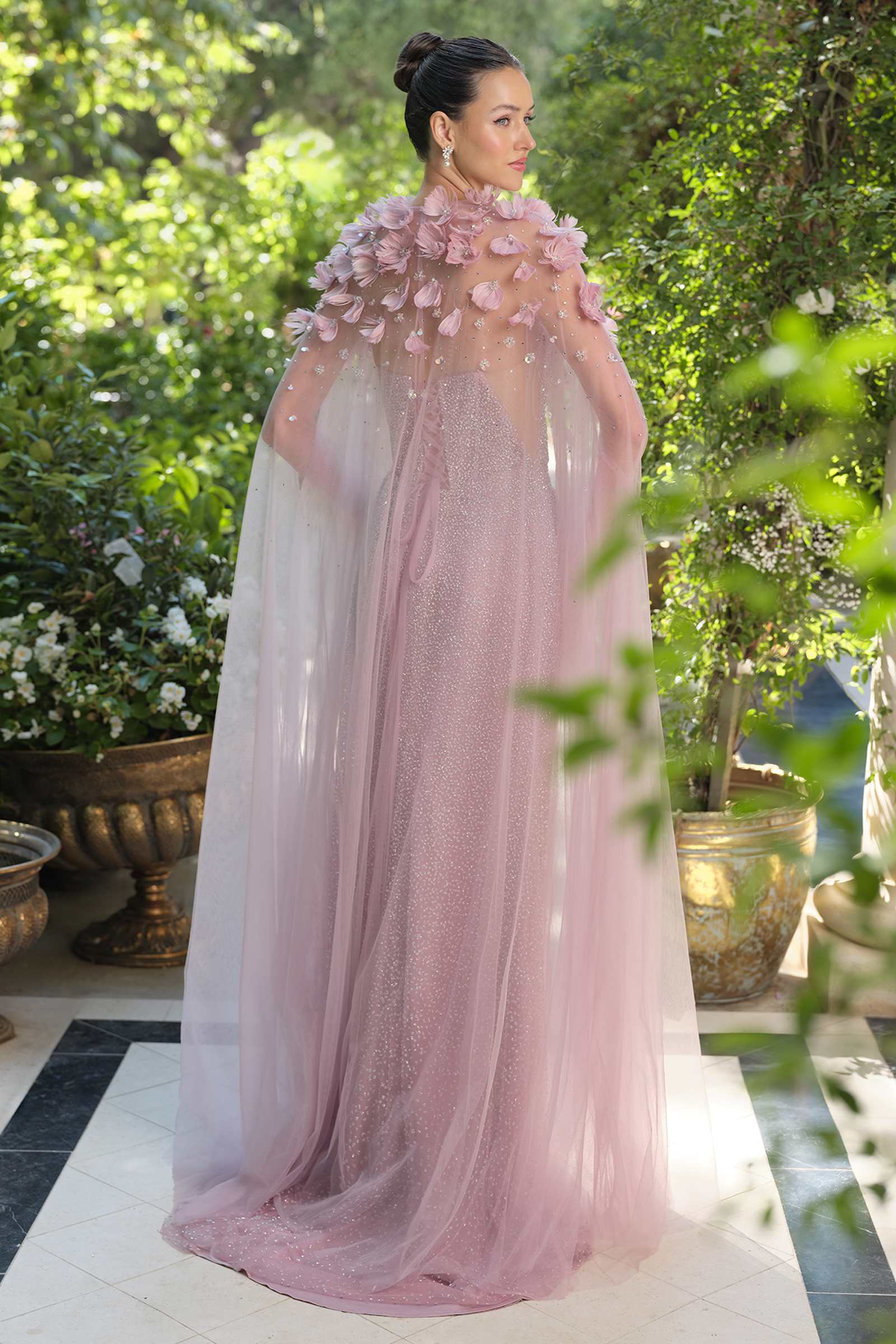 Woman in a pink floral gown standing outdoors with greenery in the background