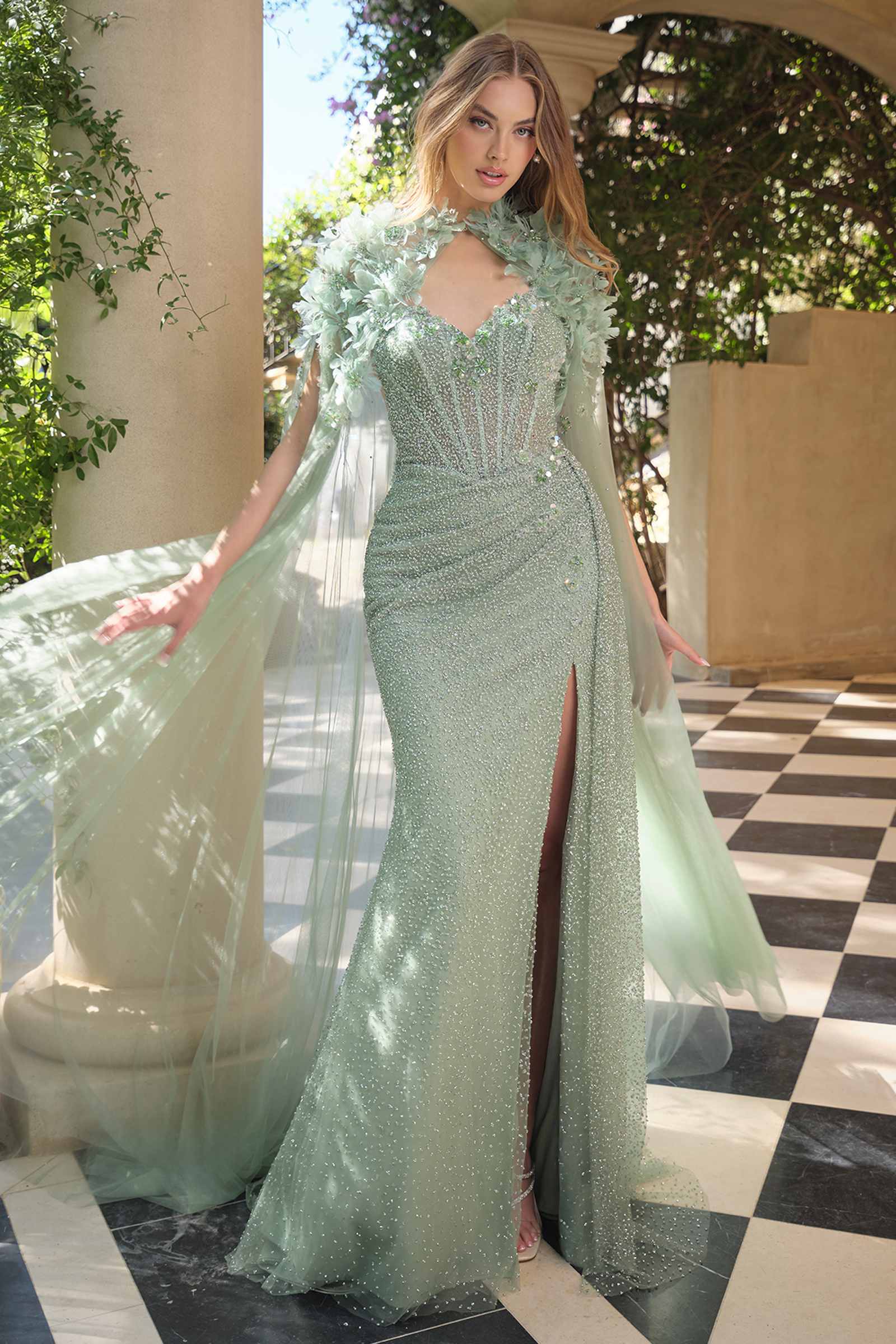 Woman in a green evening gown standing on a checkered floor with columns and greenery in the background