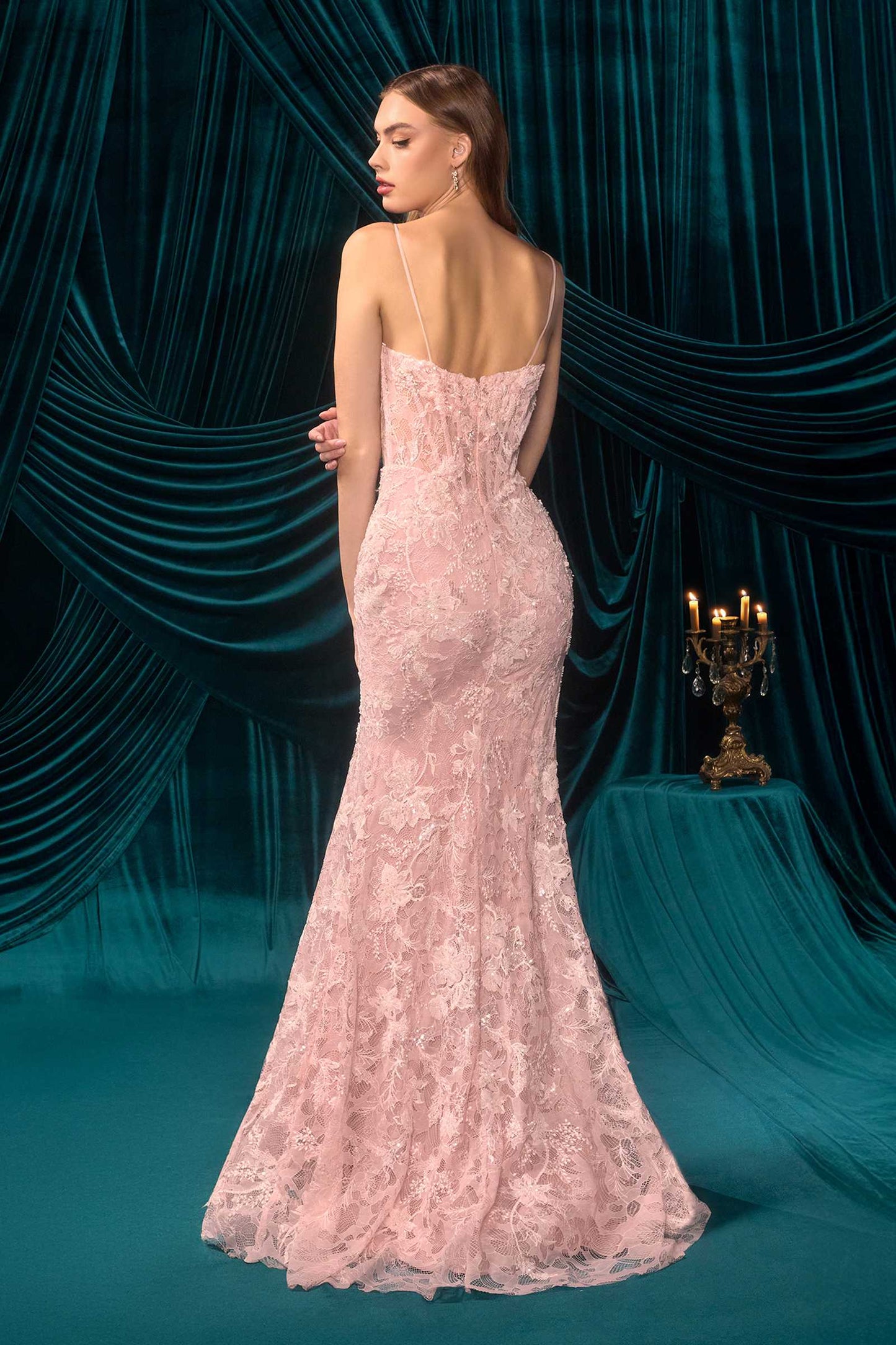 Woman in a pink lace evening gown standing against a teal curtain backdrop