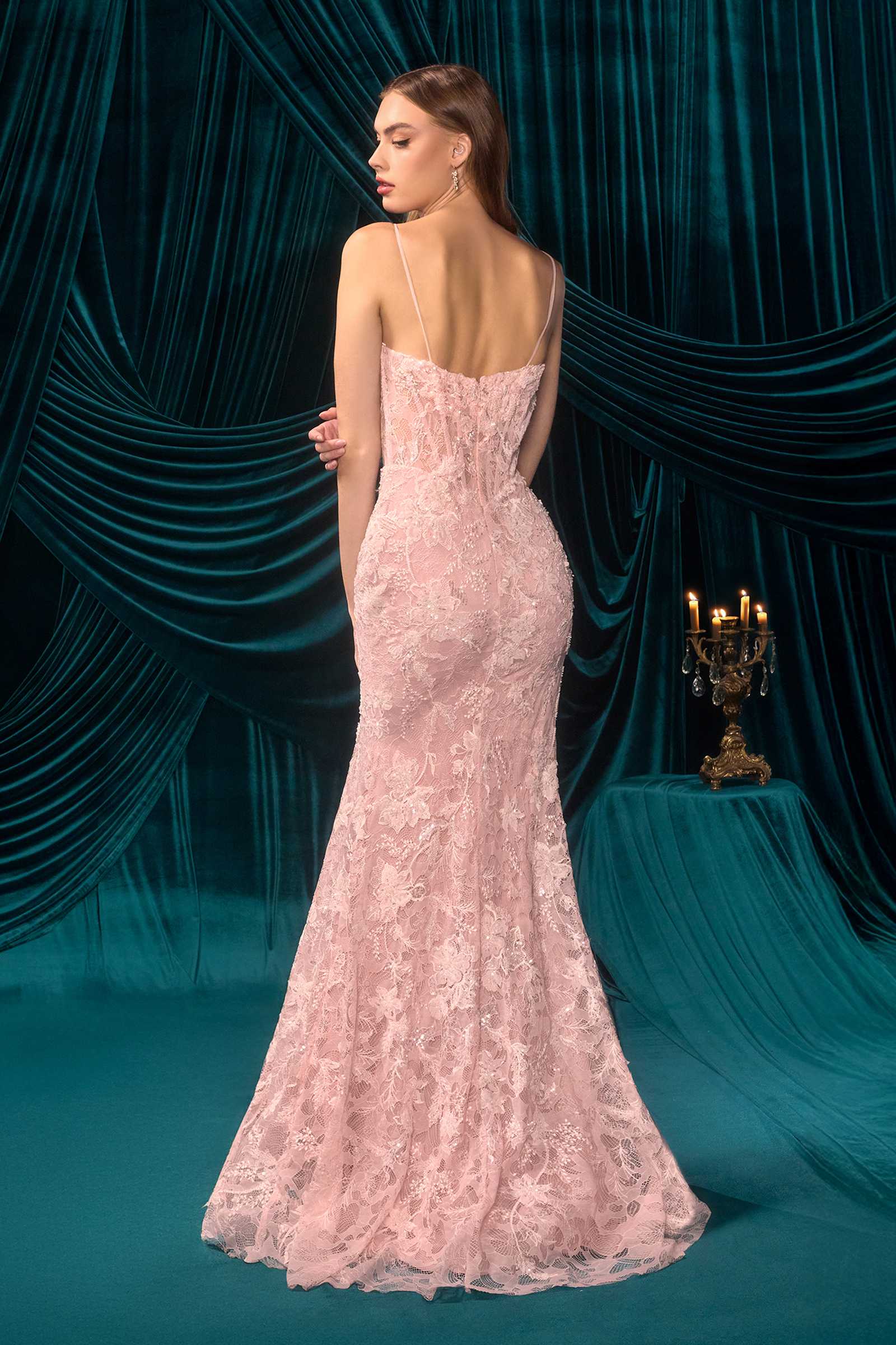 Woman in a pink lace evening gown standing against a teal curtain backdrop
