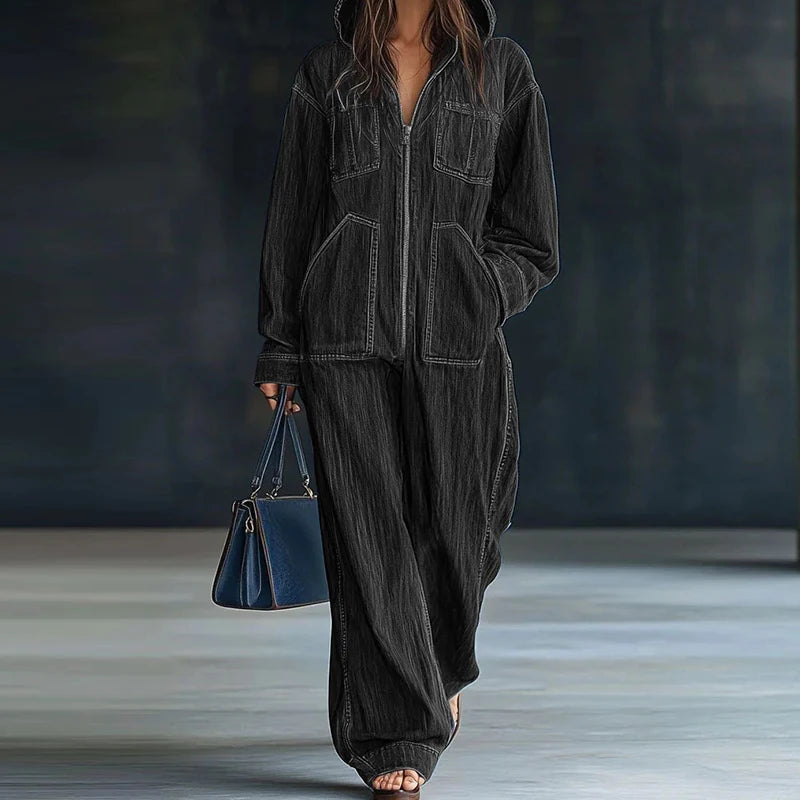 Person wearing a dark gray hooded outfit holding a blue handbag against a dark background