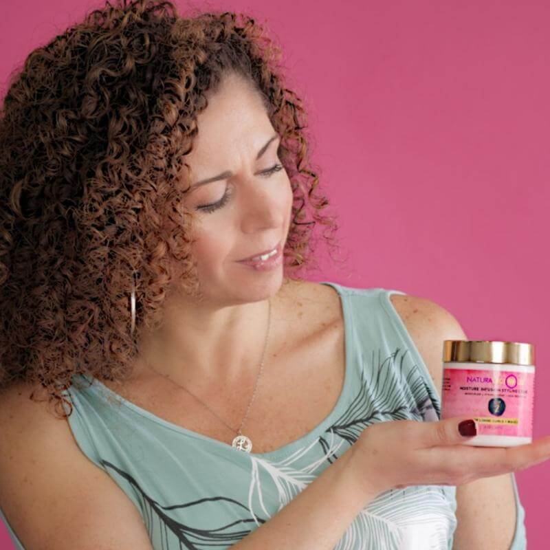Woman holding a pink jar with a gold lid against a pink background