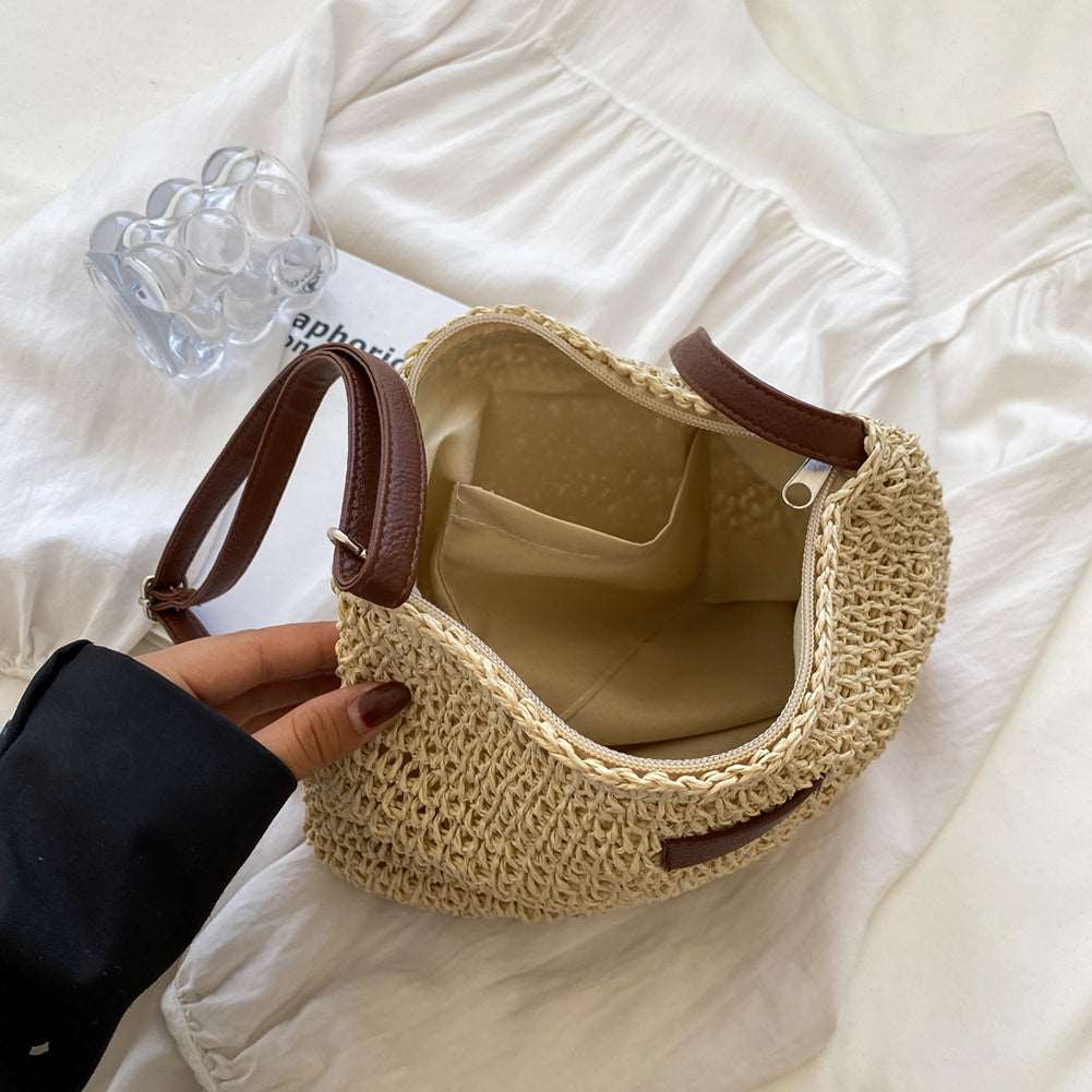 A person holds the HalleBeauty Vacation Straw Tote Bag, a stylish & spacious beach bag for travel, with brown leather handles open on a white surface. Inside, its empty with a beige fabric lining. Nearby are a translucent ring accessory and a folded white shirt.