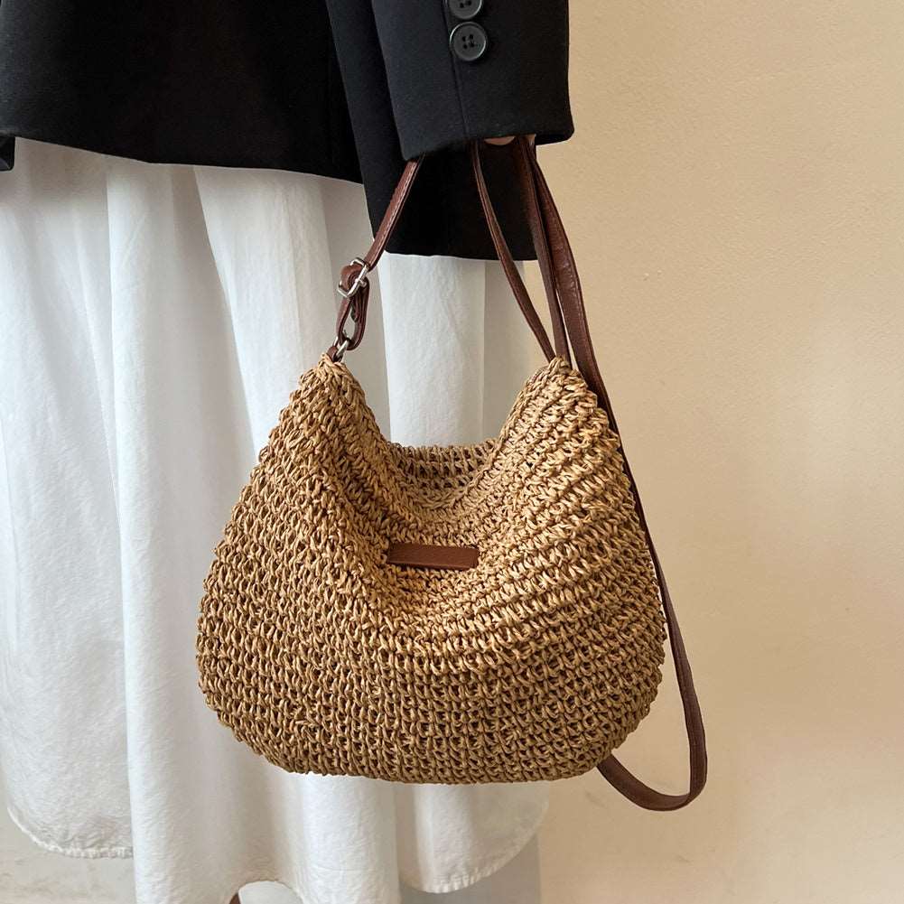 In a beige setting, someone in a white skirt and black jacket holds HalleBeautys Vacation Straw Tote Bag, a tan woven accessory with brown straps, ideal for beach trips.