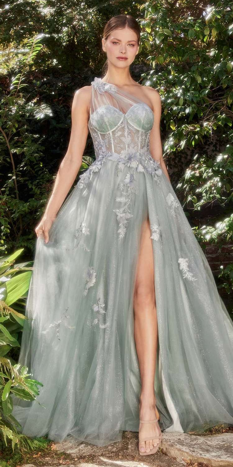 Woman in a light blue evening gown with floral details standing in a forest setting.