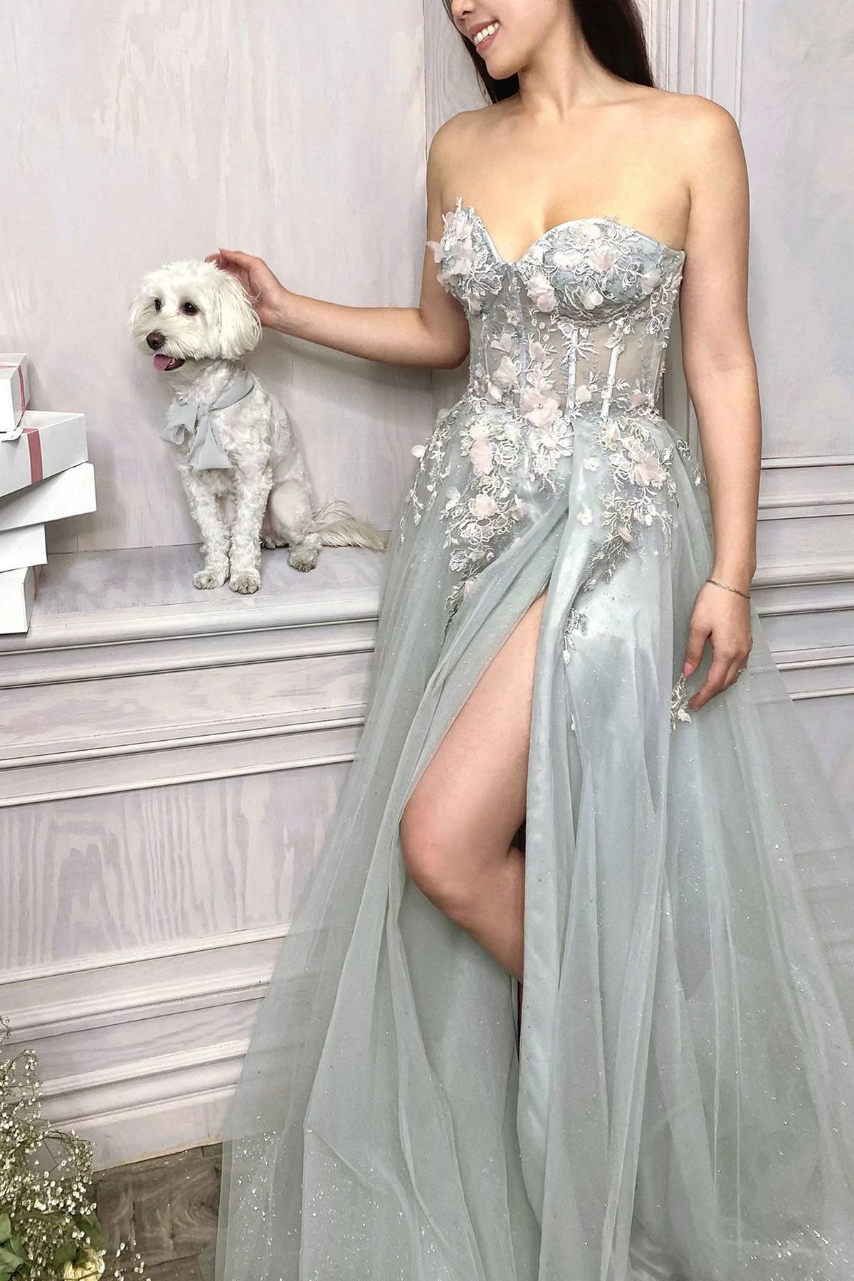 Woman in a strapless silver evening gown with a dog on a white surface.